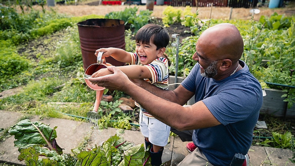 Чоловік допомагає всміхненій дитині поливати в садку рослини