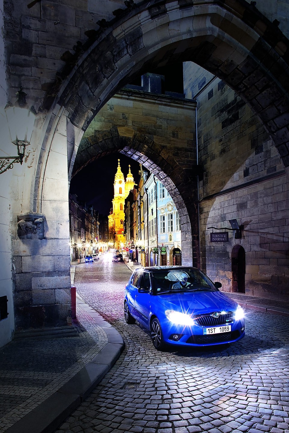 Синій автомобіль стоїть вночі під аркою на брукованій празькій дорозі