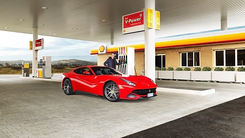 Червоний Ferrari стоїть на АЗС Shell, чоловік спирається на бензоколонку