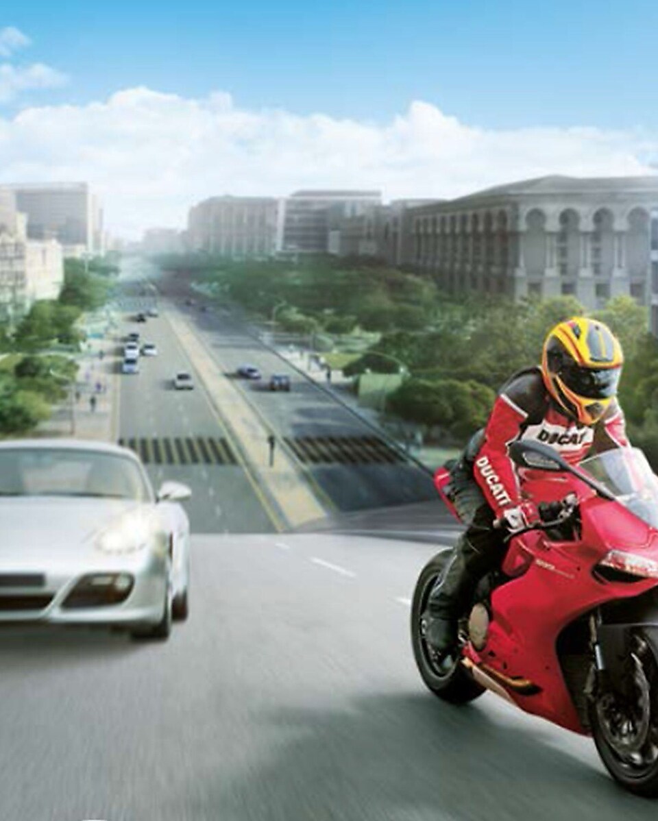 Червоний мотоцикл і мотоцикліст на дорозі з автомобілями і будівлями на задньому плані